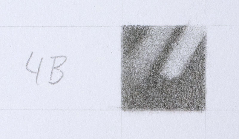 Two erasures on a swatch of 4B applied with moderate pressure. Kneaded eraser on the left, a Tombow Mono Zero stick eraser on the right.